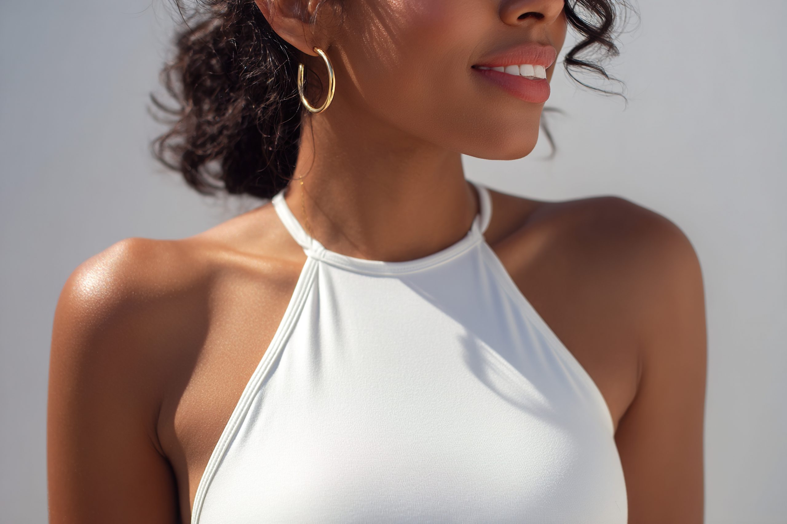 Close de mulher com body branco de alças finas e argolas douradas, em estilo leve e sofisticado.